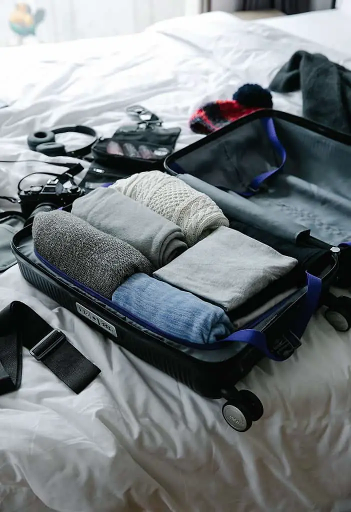 Various travel essentials neatly arranged on a wooden surface, including passport, maps, camera, clothing, and a backpack, representing the ultimate packing checklist for adventurers.