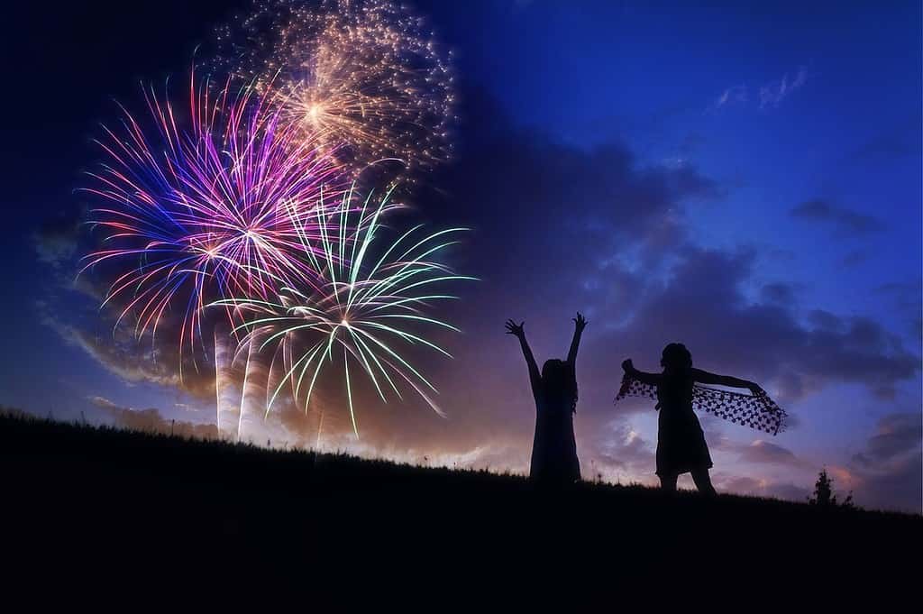 2 girls standing on a hill watch fireworks at night 