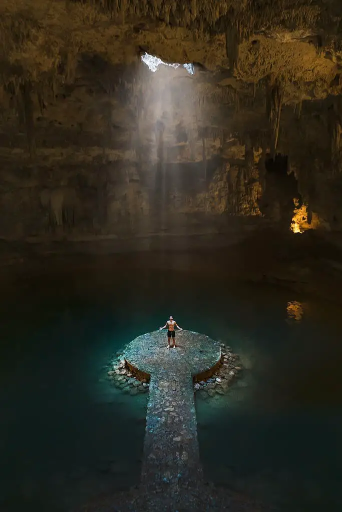 Man Standing in the middle of a cenote with light shinning down of him