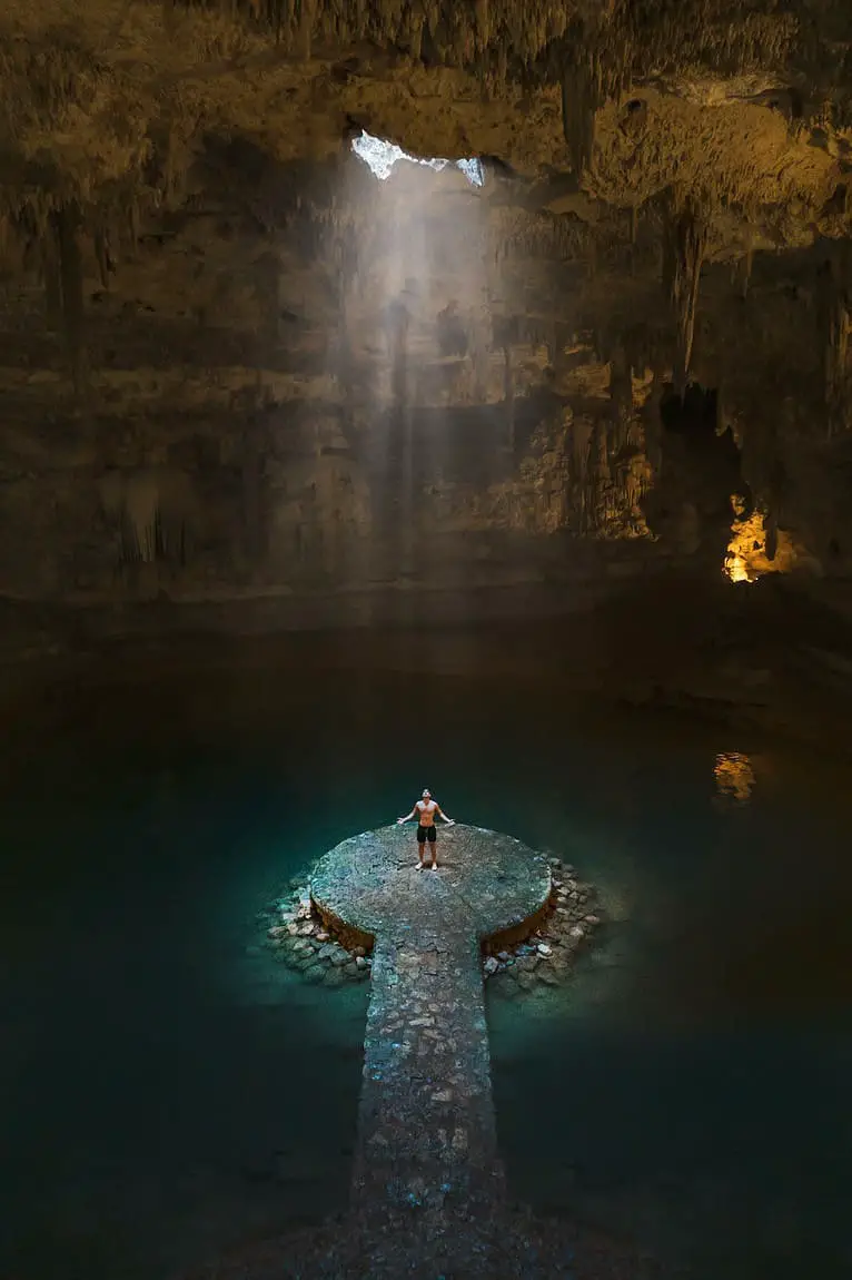 Man Standing in the middle of a cenote with light shinning down of him